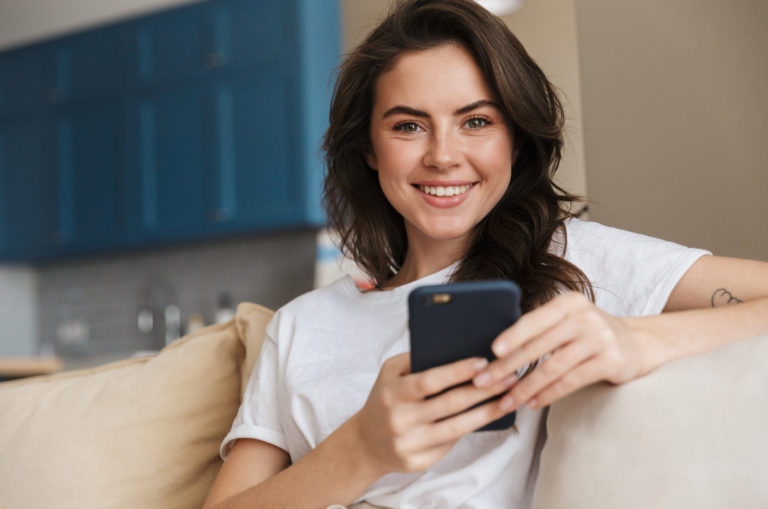 smiling young woman with smartphone on the couch