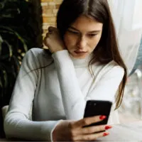 a woman with long brown hair sits at a table and buttons on the phone