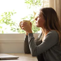 an imaginary woman sitting at a table drinking coffee and looking out the window