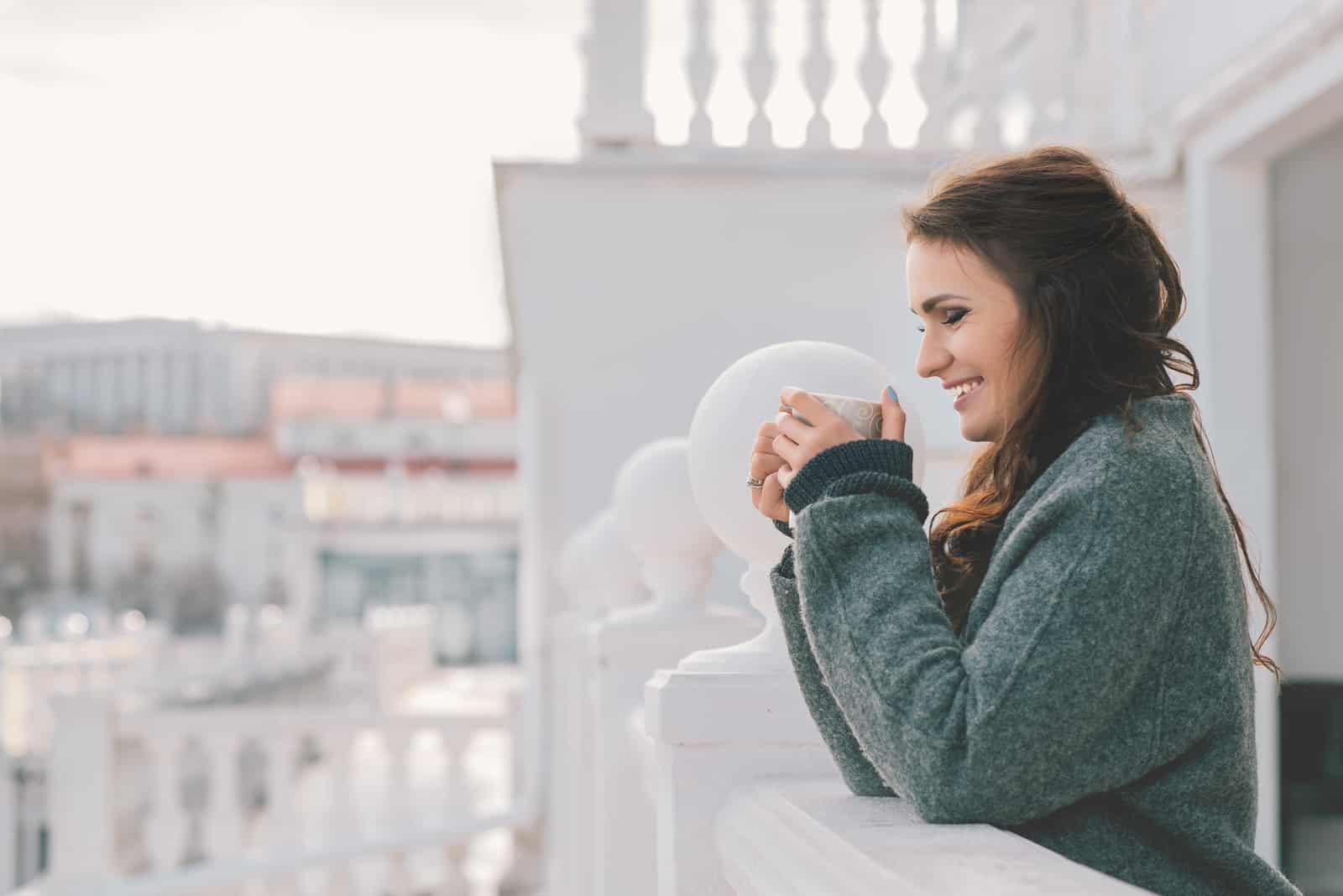a smiling woman drinking coffee on the balcony