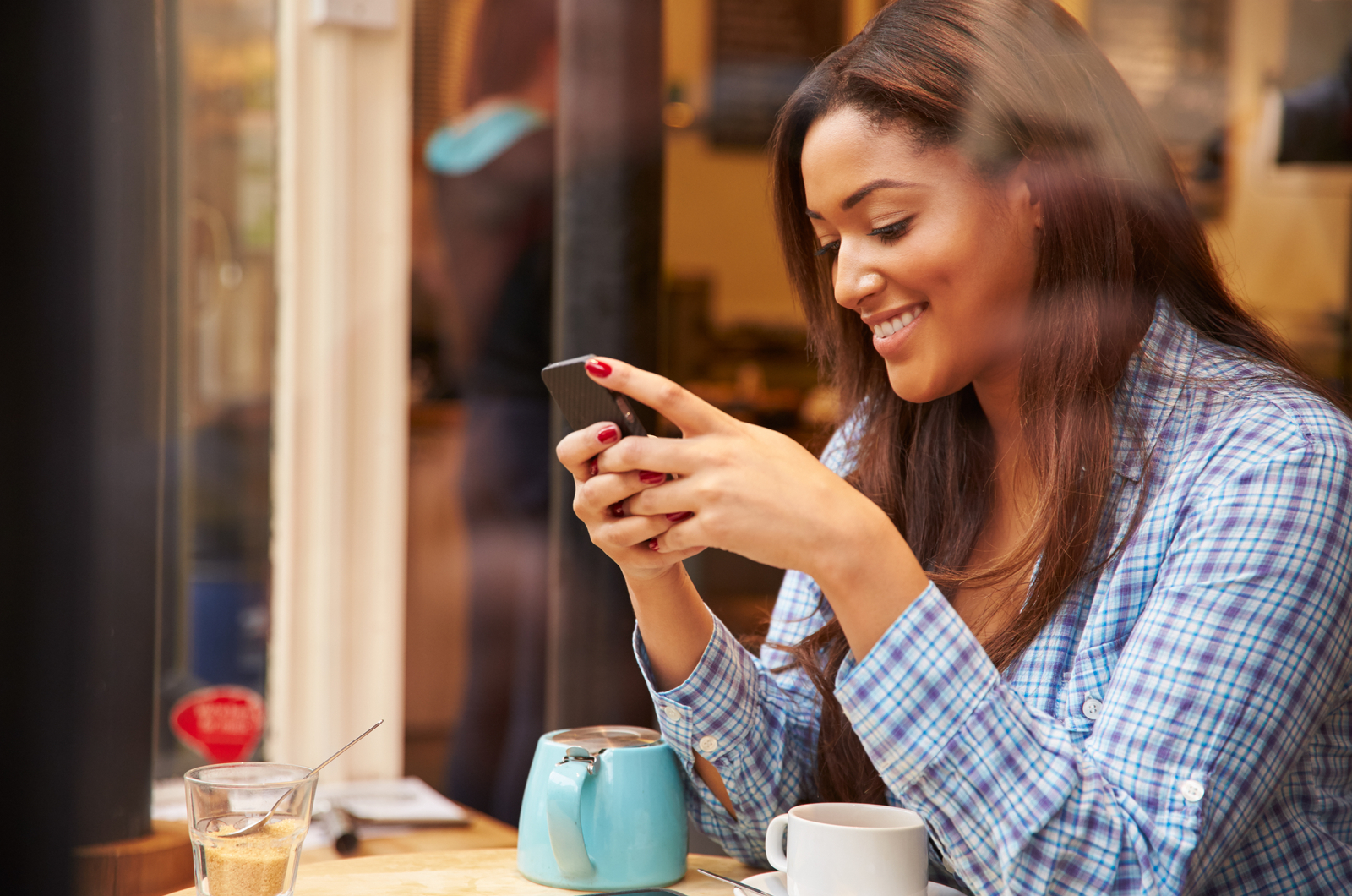 una mujer sonriente sentada en un café y tecleando en el teléfono