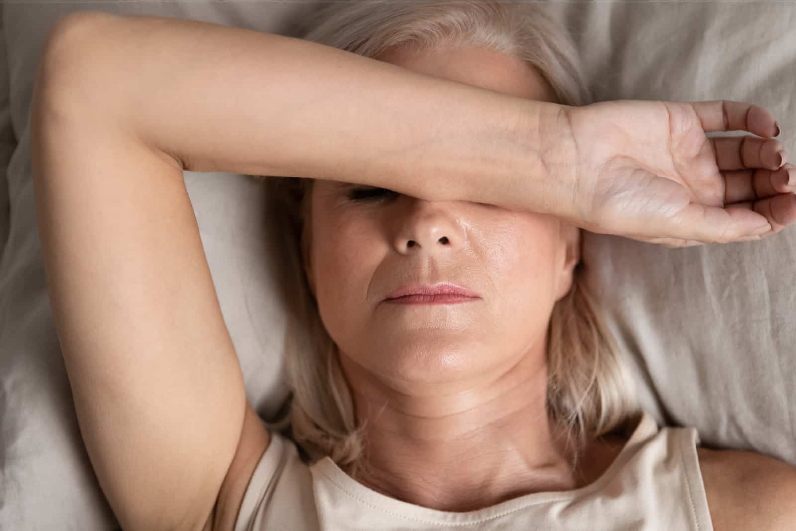 middle-aged woman lying down in bed on pillow putting hand on face