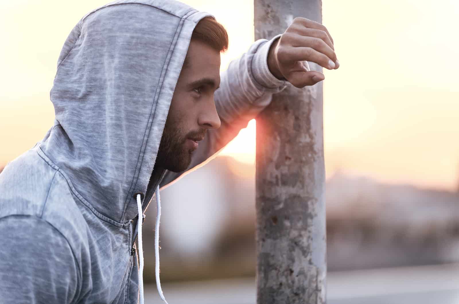 thoughtful young man wearing hood and looking away