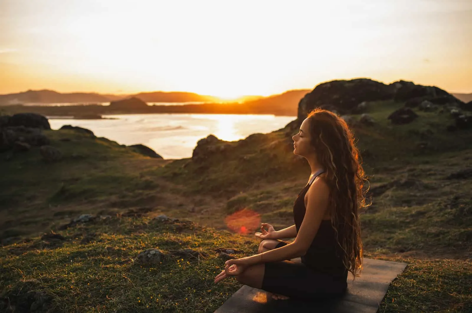 woman meditating on rocks by sea