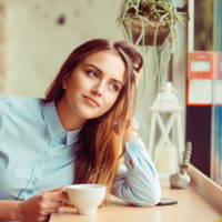 pensive woman sits at the table and drinks coffee