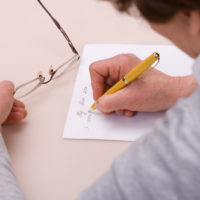 una mujer sostiene unas gafas en la mano mientras escribe una carta
