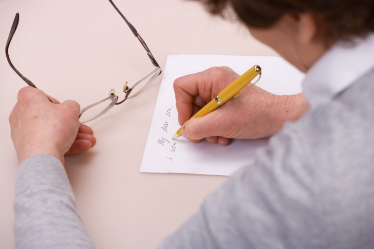 a woman holds glasses in her hand while writing a letter