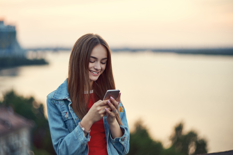 a smiling girl is standing and typing on the phone