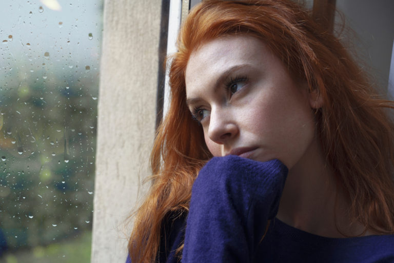 pensive woman sits by the window