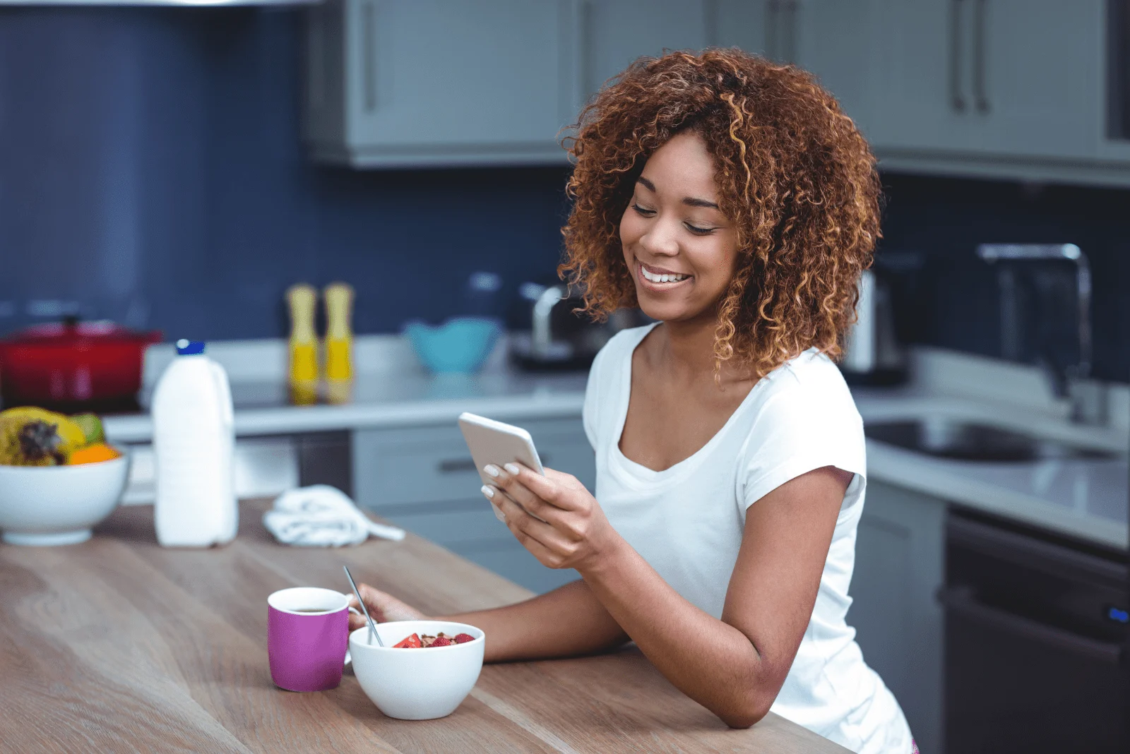 a smiling woman is sitting in the kitchen and typing on the phone