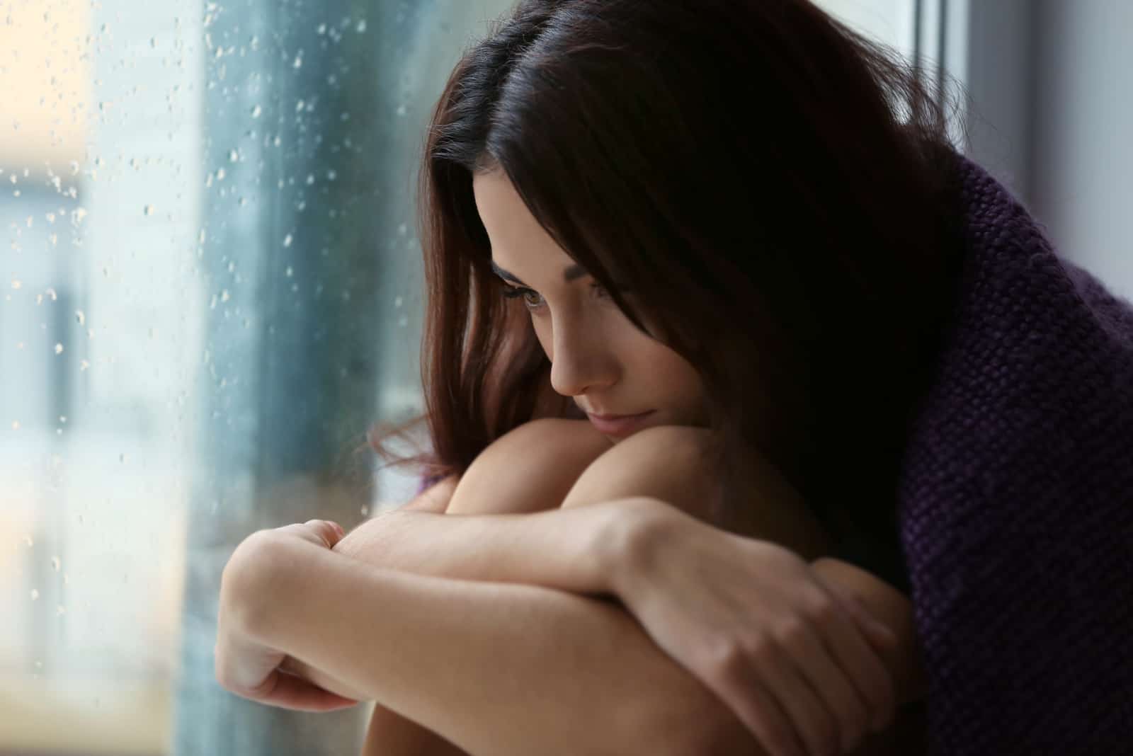 a woman with long black hair sits by the window