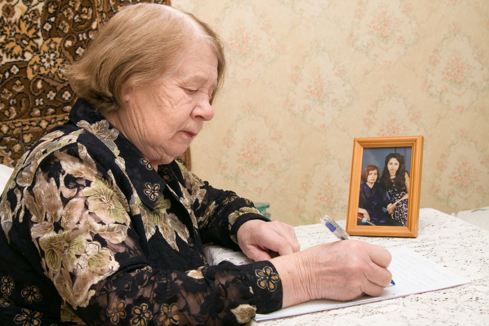 an elderly woman sits at a table and writes a letter
