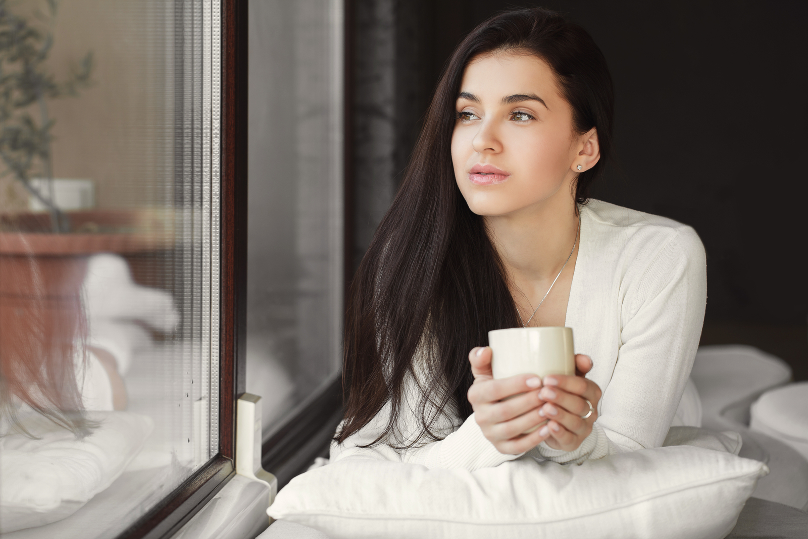donna carina che beve una tazza di caffè vicino alla finestra