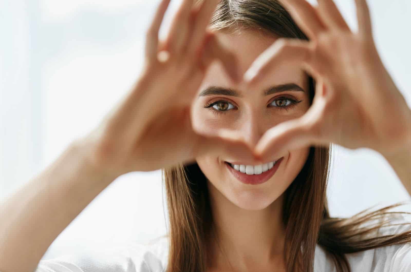 happy woman holding heart shaped hands near eyes