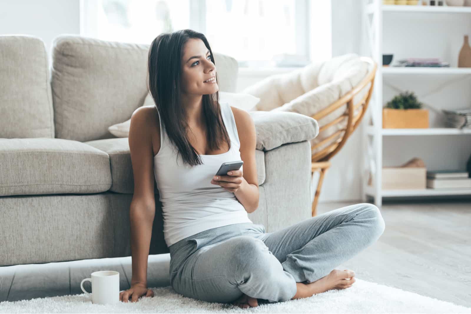 mulher feliz sentada no chão com o telemóvel na mão