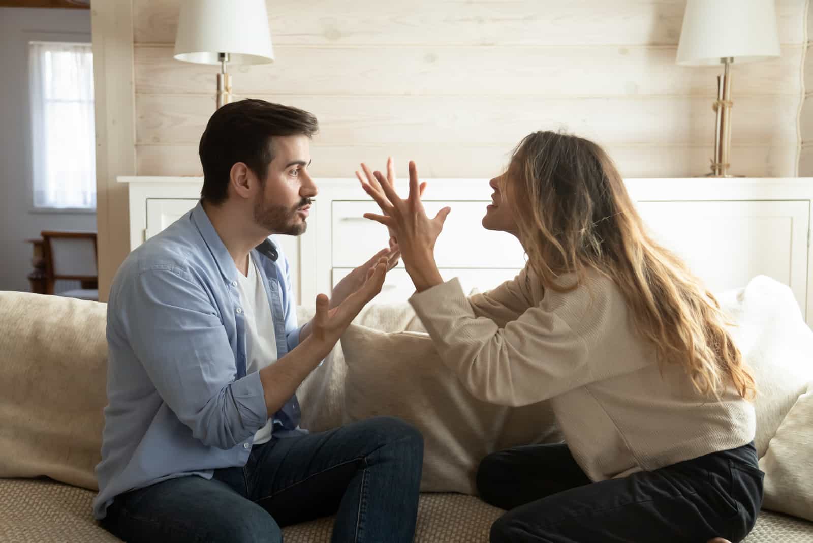 stressed couple sitting on couch, arguing at home.