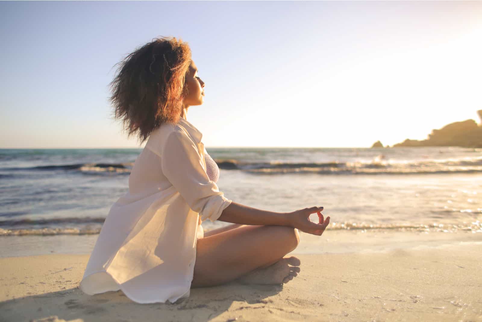woman meditates on the beach in sunlight
