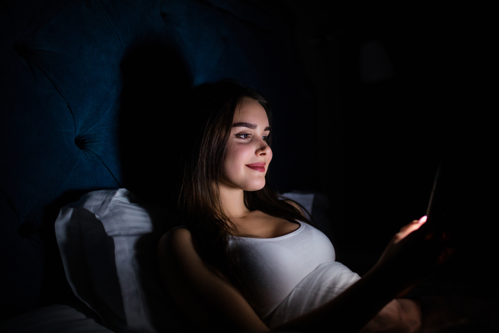 mujer joven tumbada en la oscuridad enviando mensajes de texto