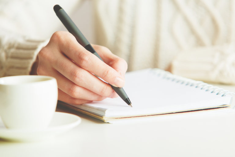 woman writing in notebook while sitting in park