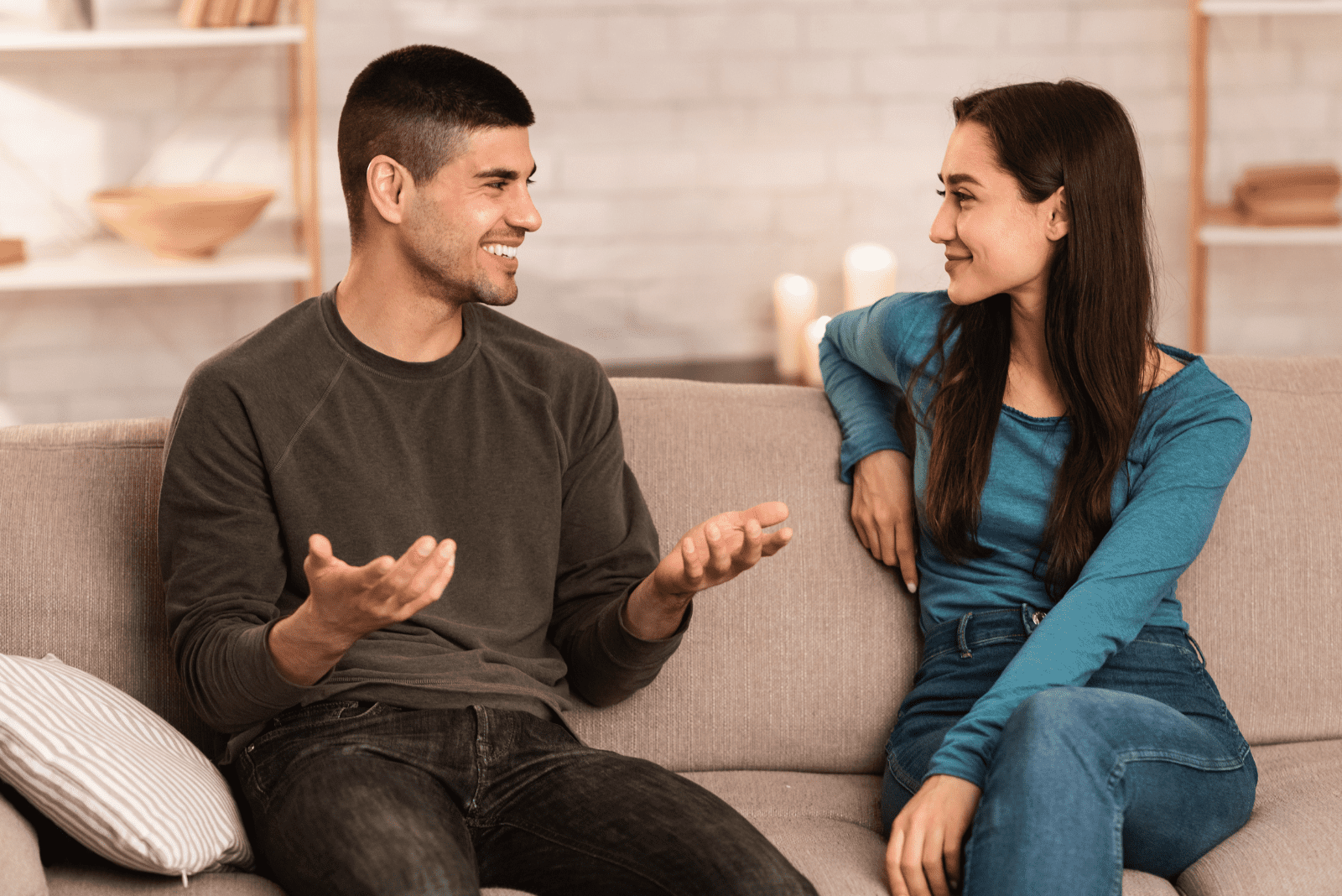 um homem sorridente está sentado num sofá e conversa com uma mulher