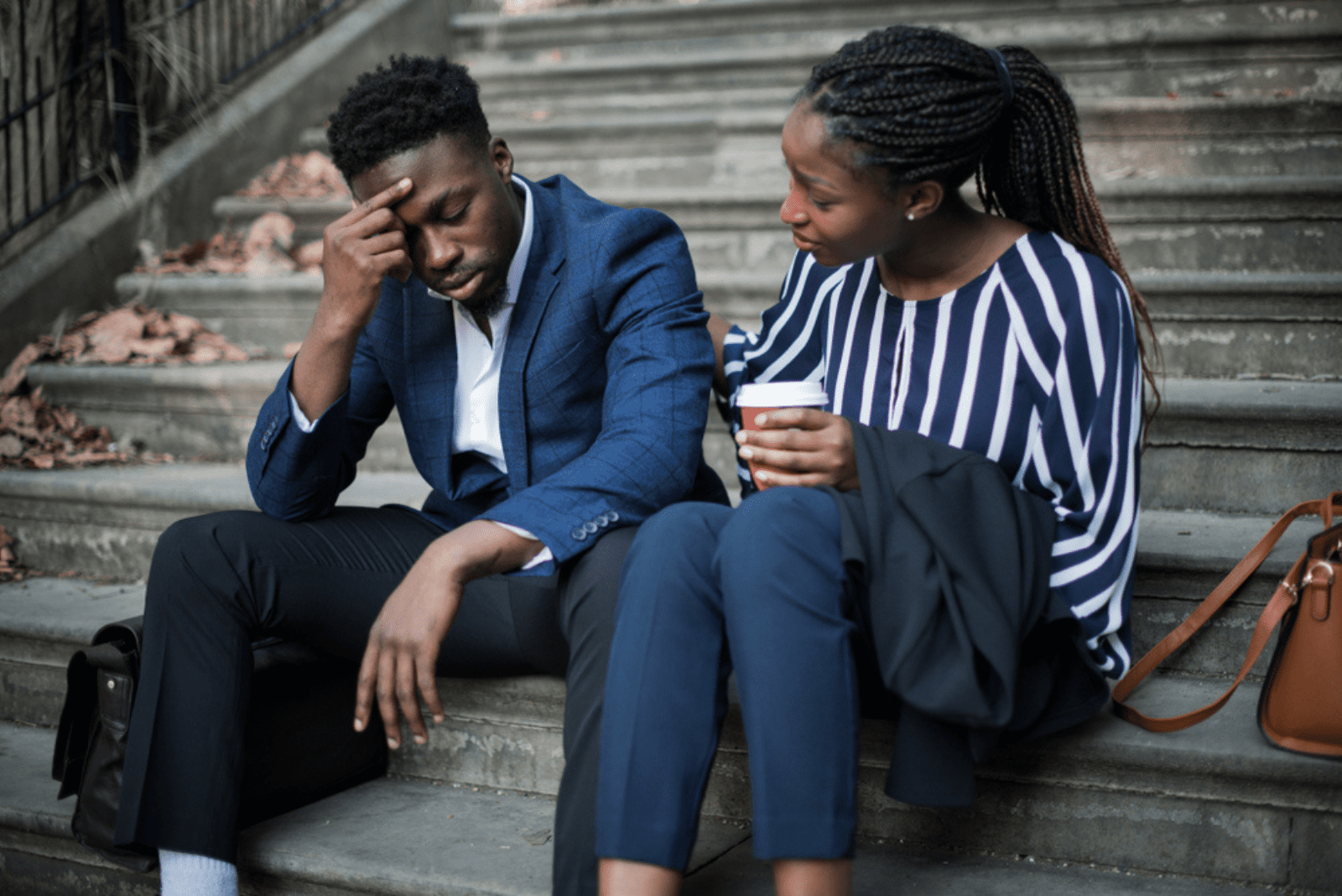 a woman comforts a man while they sit on the stairs