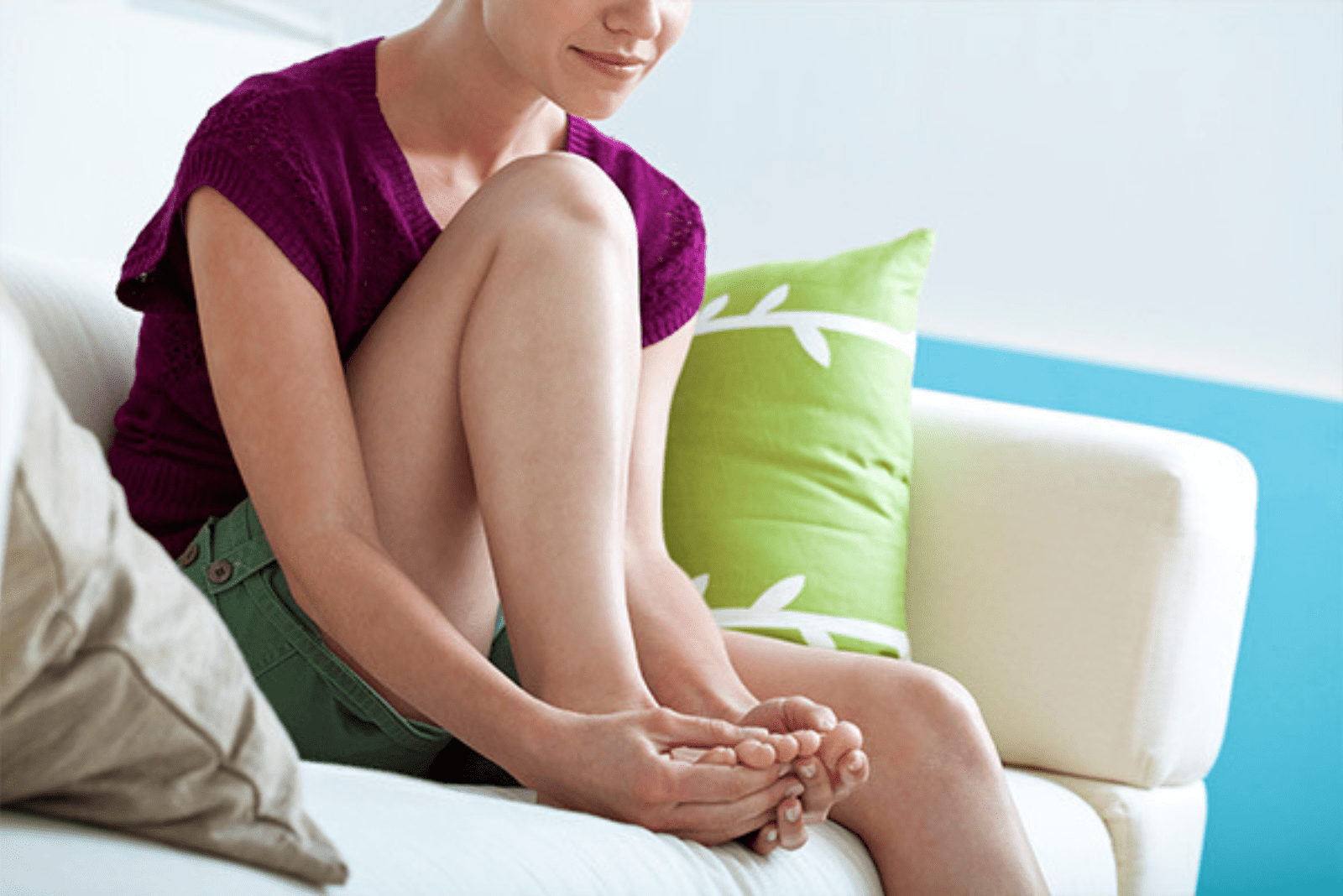 a woman is sitting on the couch and scratching her right foot