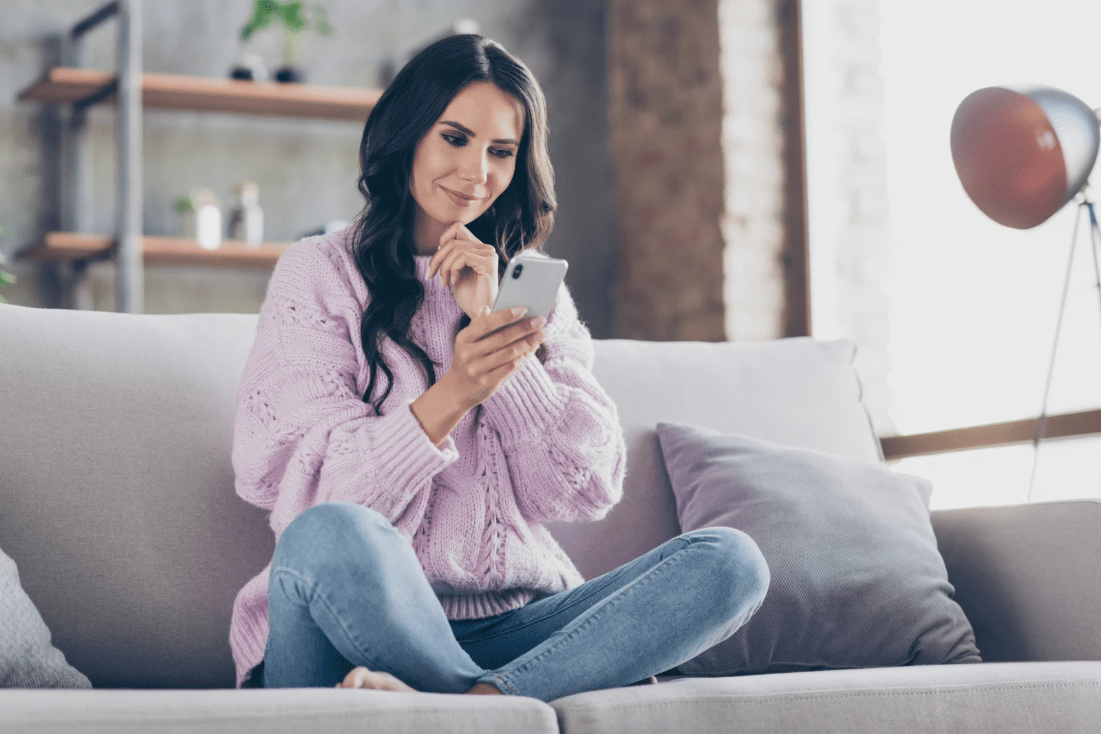 a woman with long black hair is sitting on the couch and typing on the phone