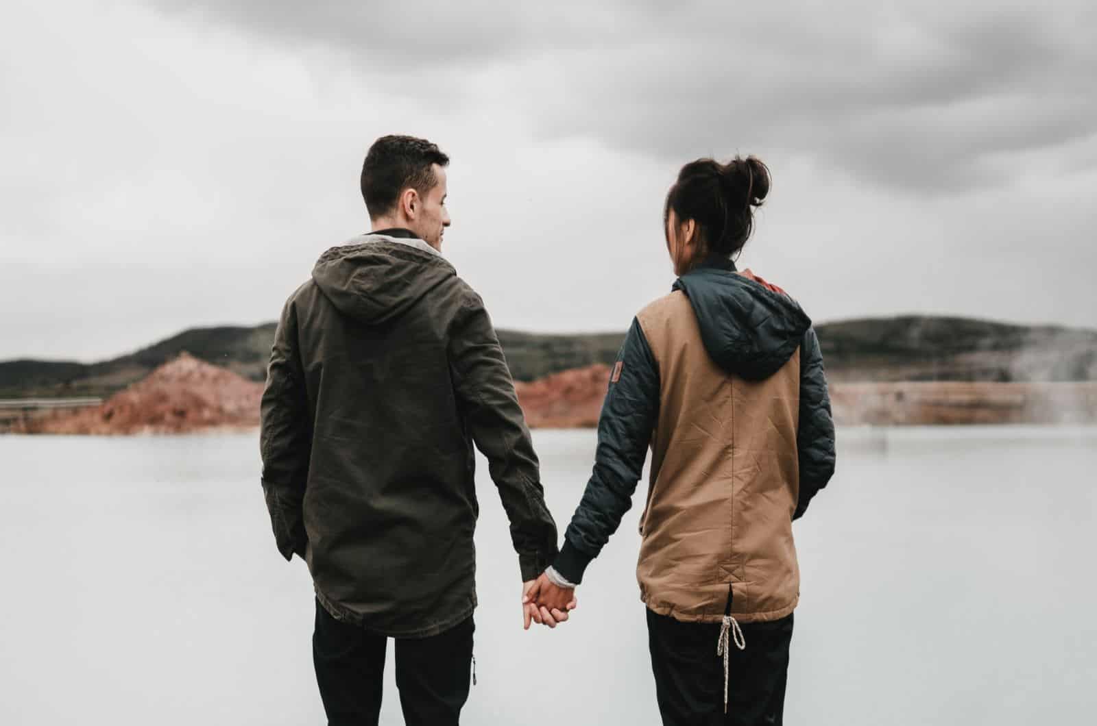 couple holding hands in front of a lake
