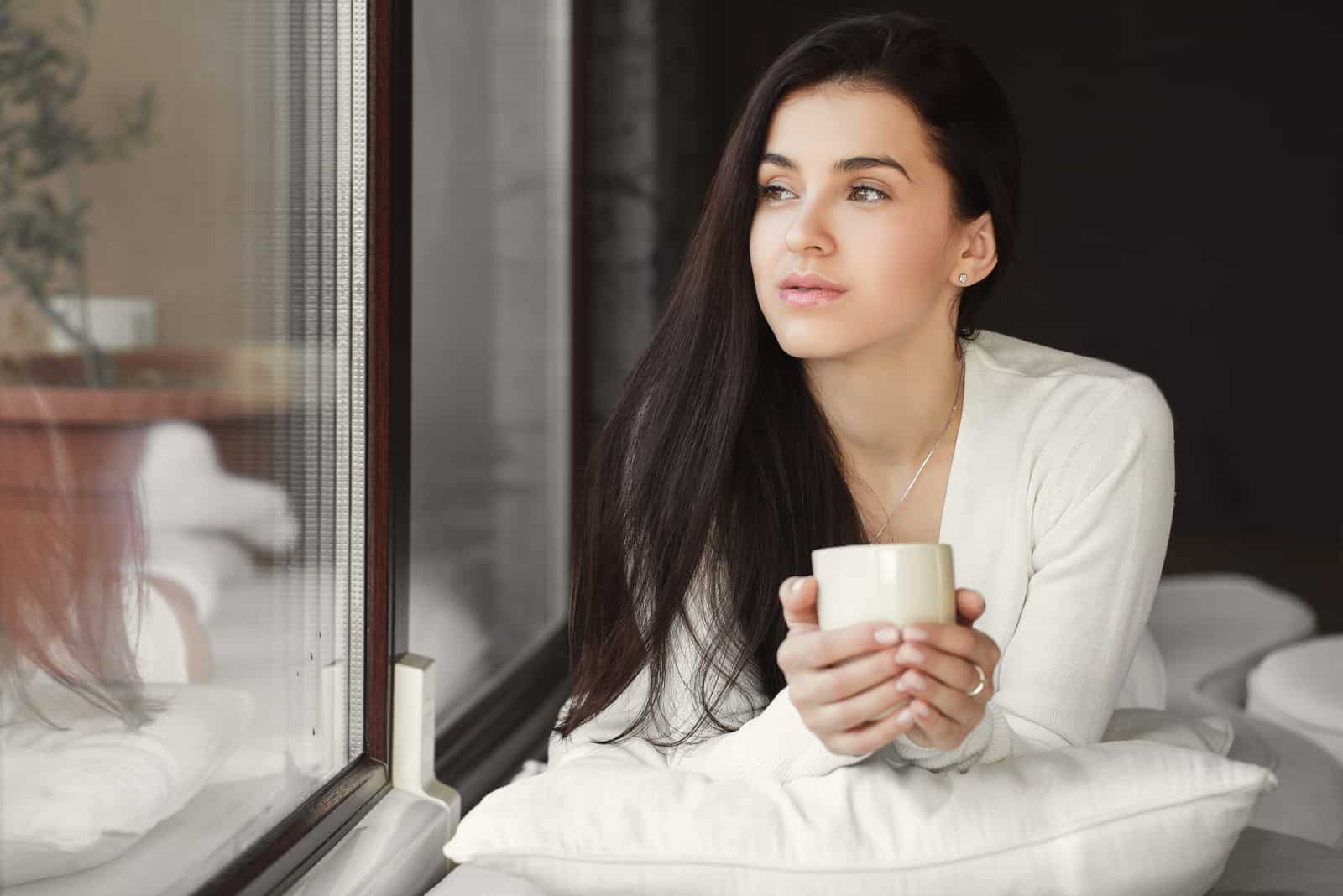 linda mujer bebiendo una taza de café por la ventana