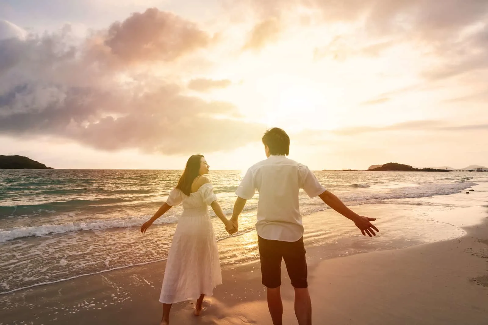 happy couple walking on beach in sunset