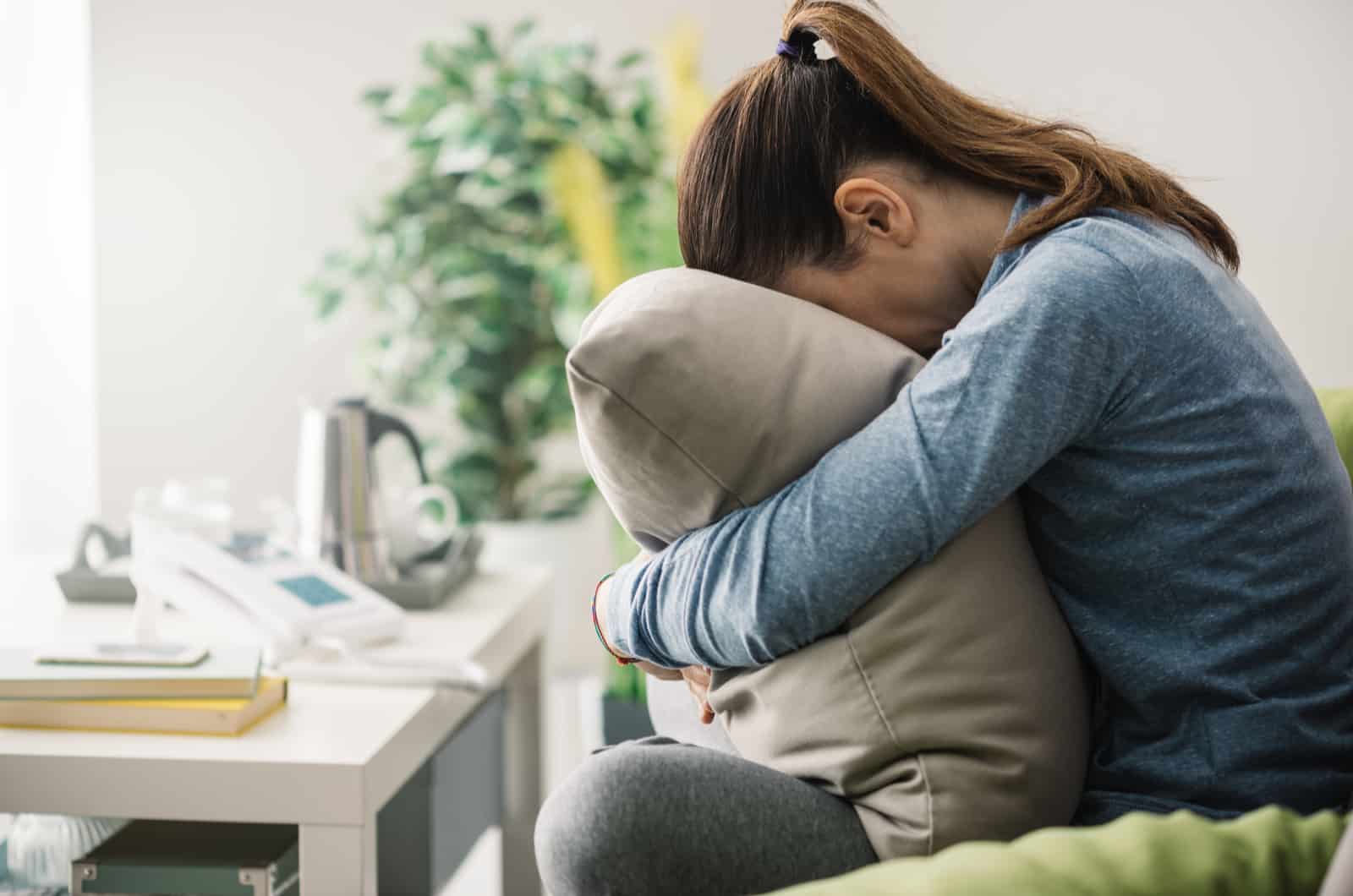 upset woman hugging pillow while sitting on sofa