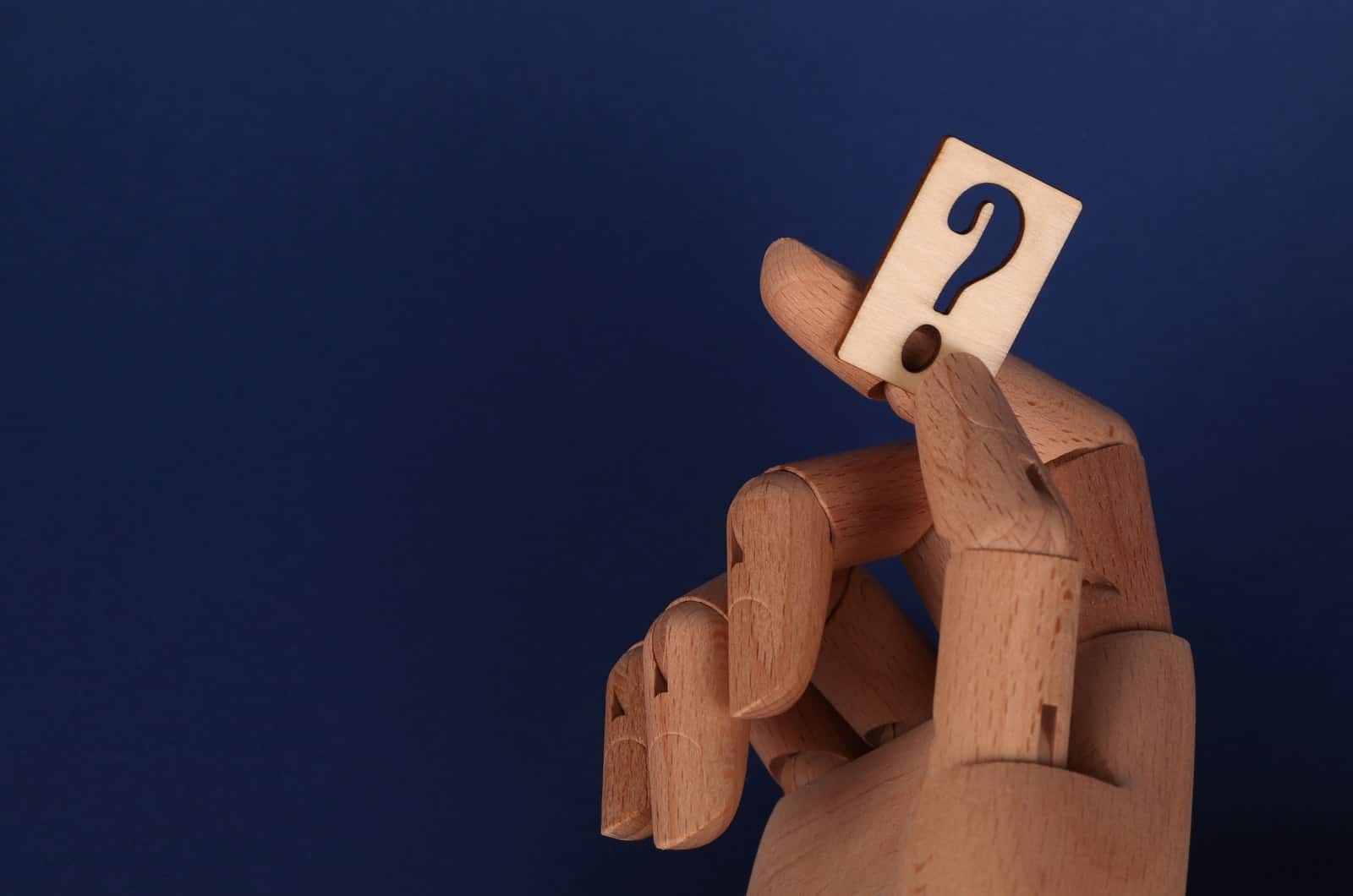 wooden hand holding a question mark