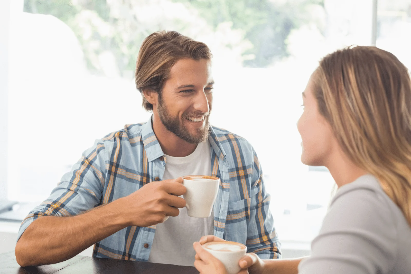 A smiling man is talking to a woman over coffee