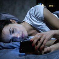 donna triste sdraiata sul letto al telefono