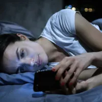 sad woman lying on bed on her phone
