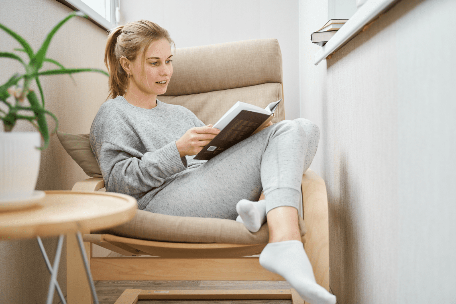 una bella donna con i capelli legati è seduta su una poltrona e sta leggendo un libro