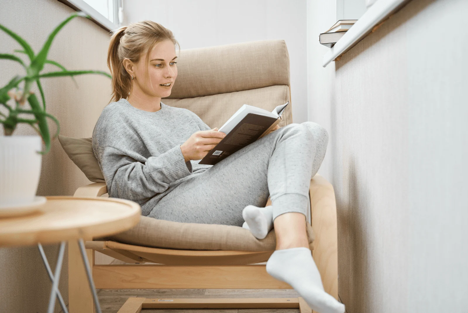 a beautiful woman with tied hair is sitting on an armchair and reading a book