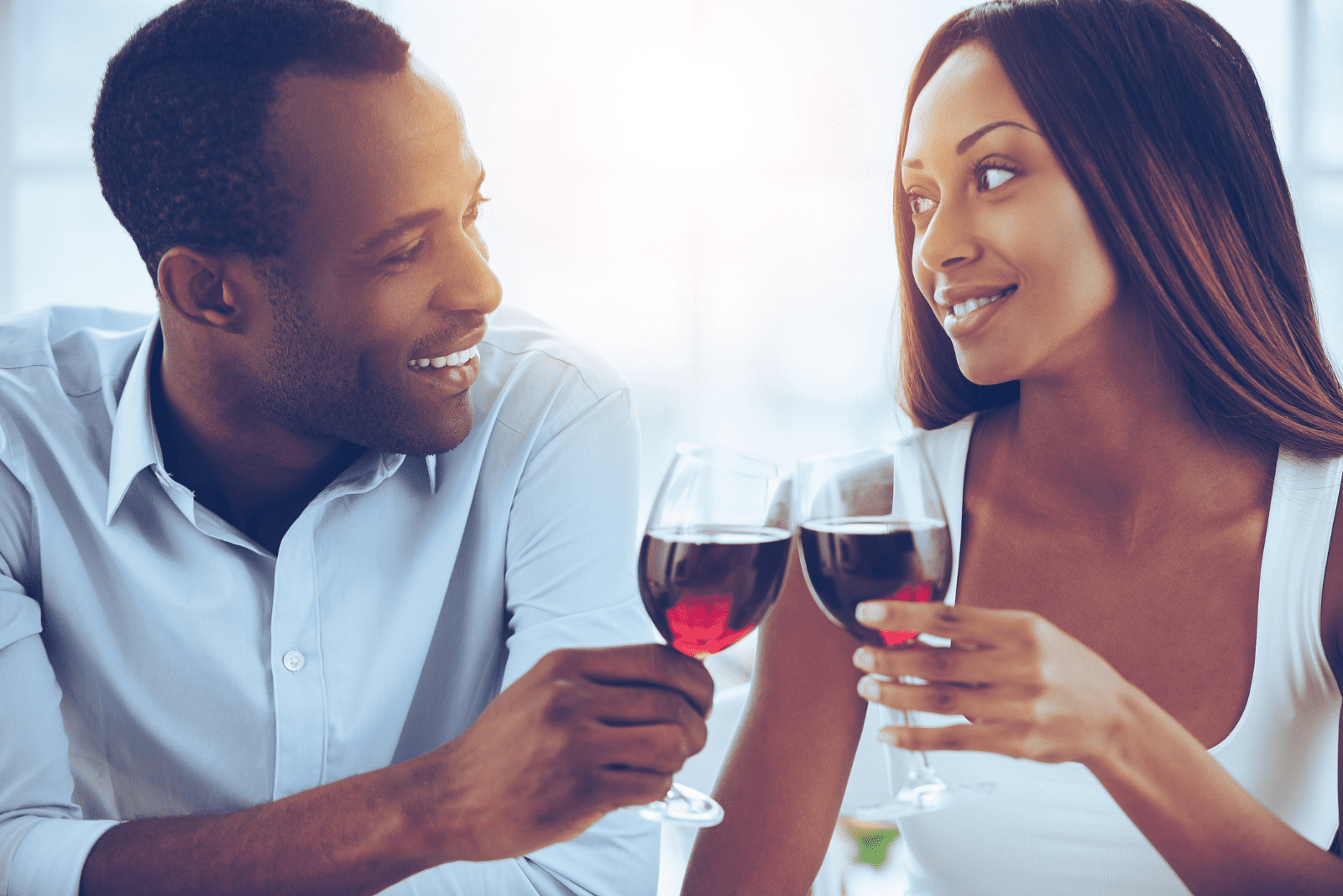 um homem e uma mulher sentam-se ao lado um do outro e brindam com vinho