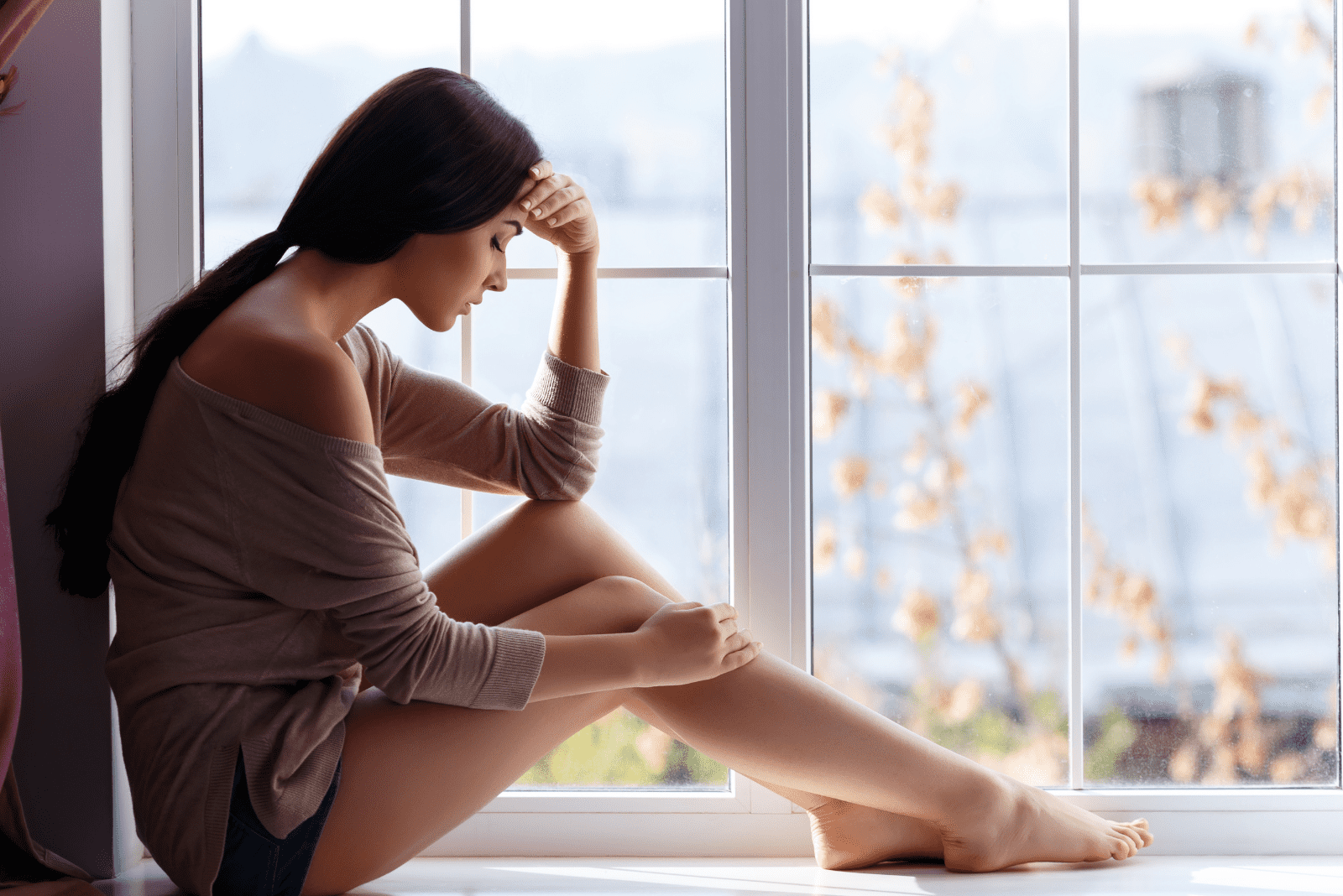 a sad woman sits by the window