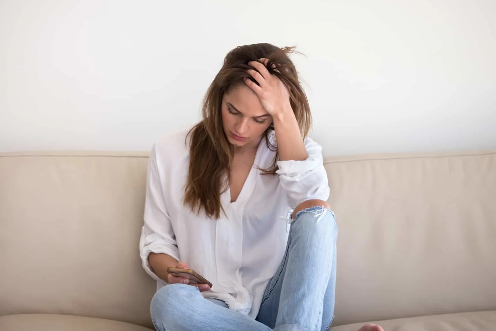 sad young woman looking at mobile phone on the couch