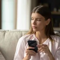 Serious thoughtful young woman holding smartphone