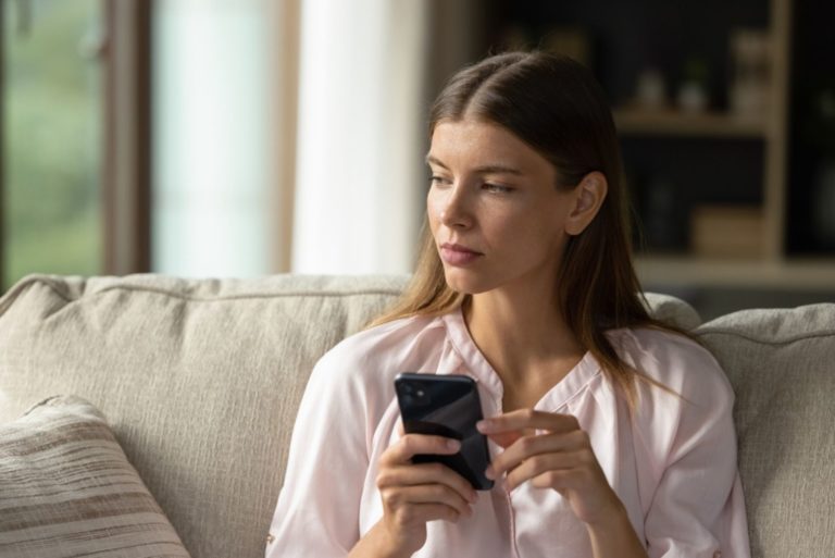 Serious thoughtful young woman holding smartphone