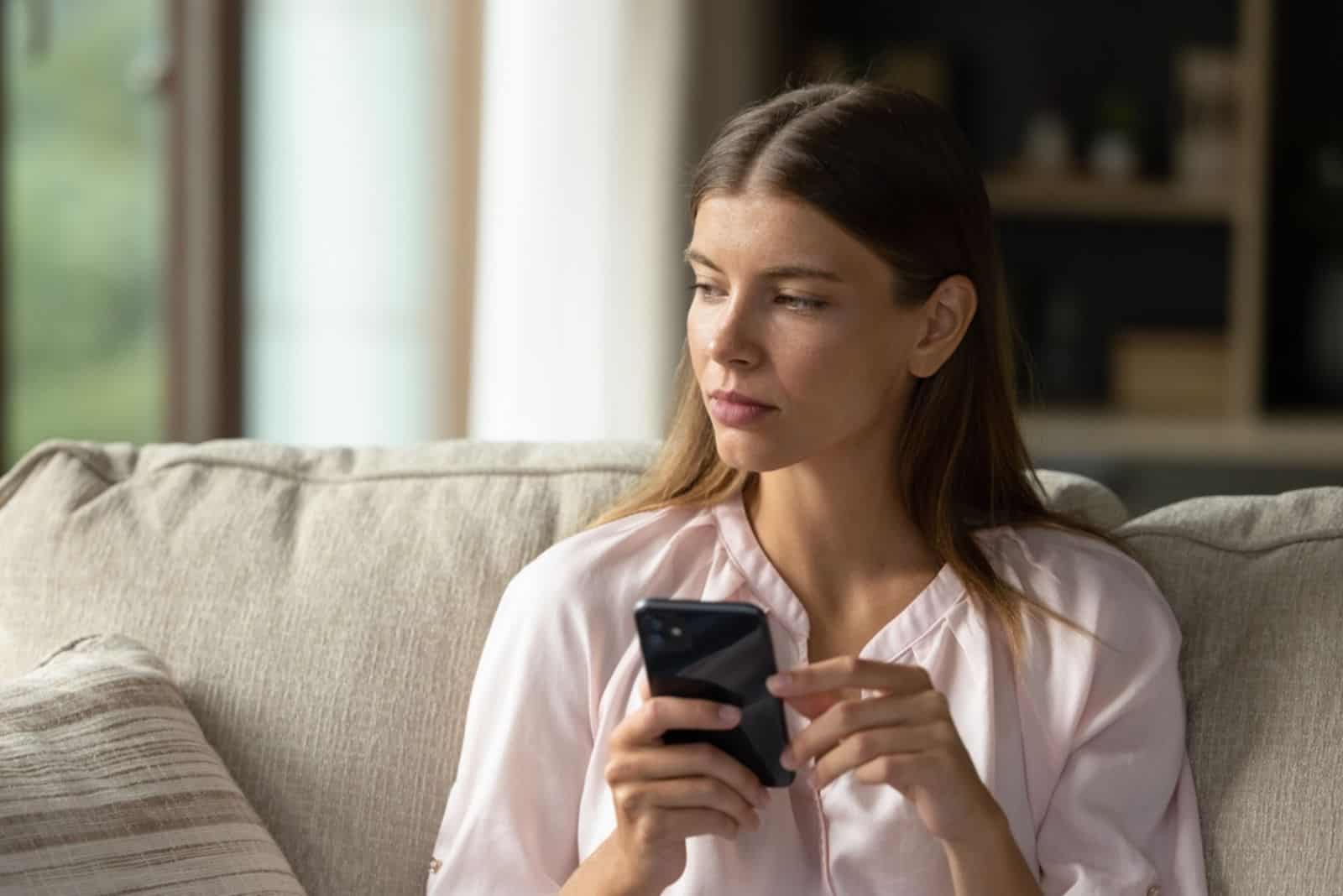 Serious thoughtful young woman holding smartphone