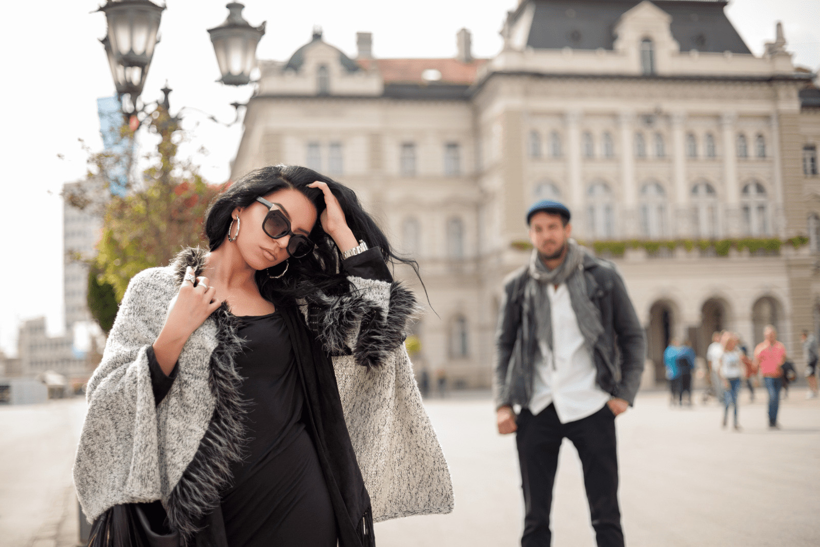 a beautiful woman stands on the street while a man looks at her