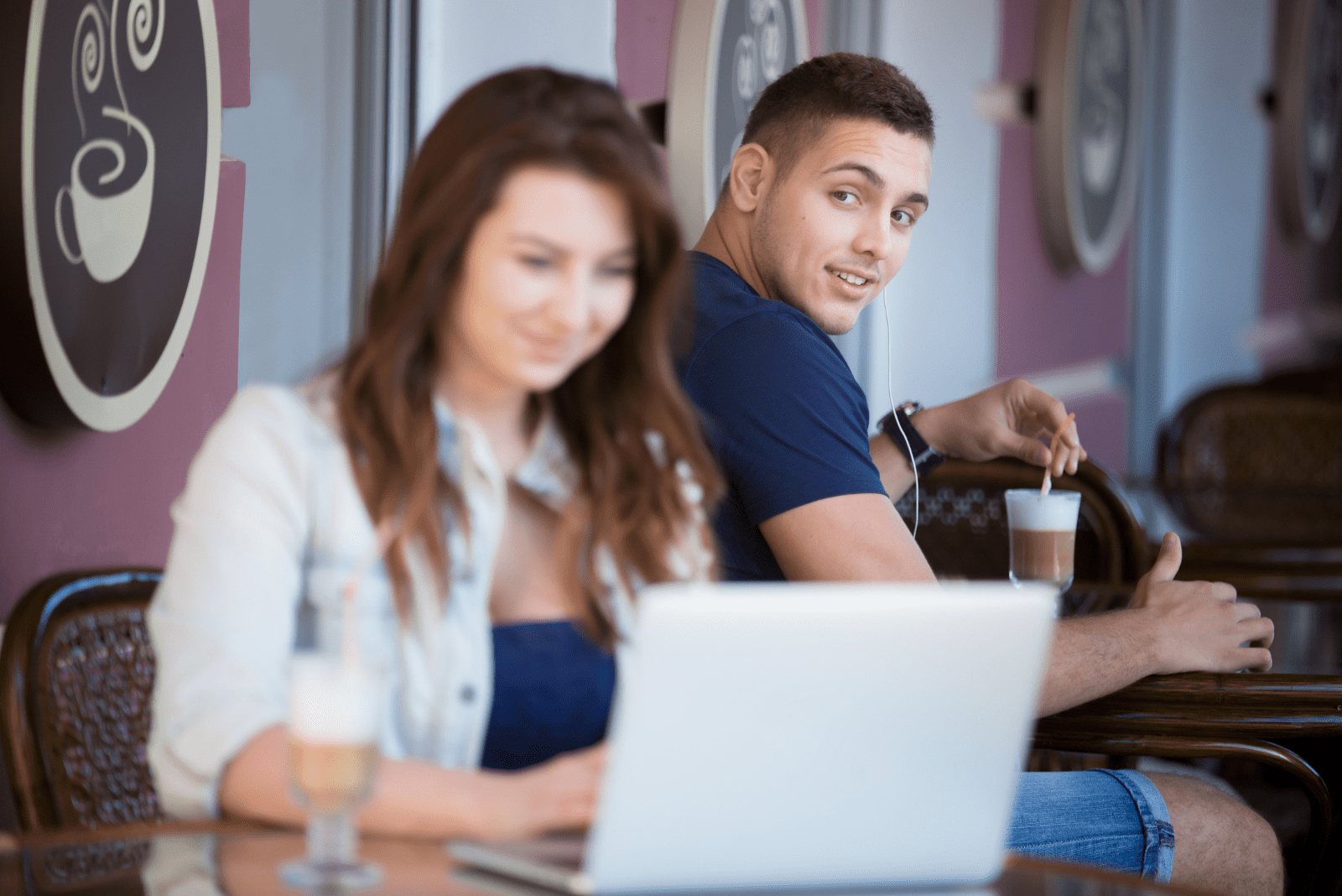 a man looks at a woman sitting in a cafe at a laptop