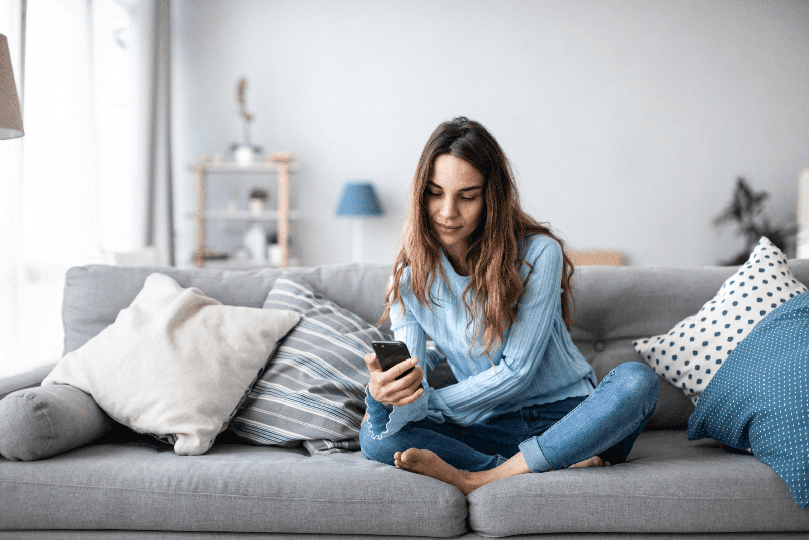 thoughtful woman sitting on the couch and typing on the phone