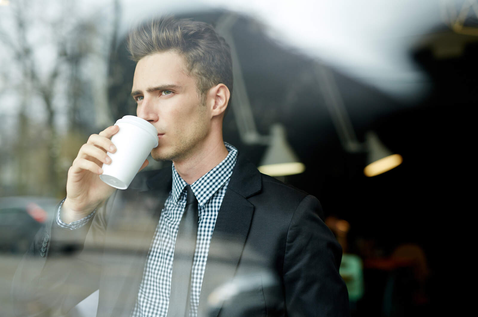 giovane uomo che beve un caffè e guarda attraverso la finestra