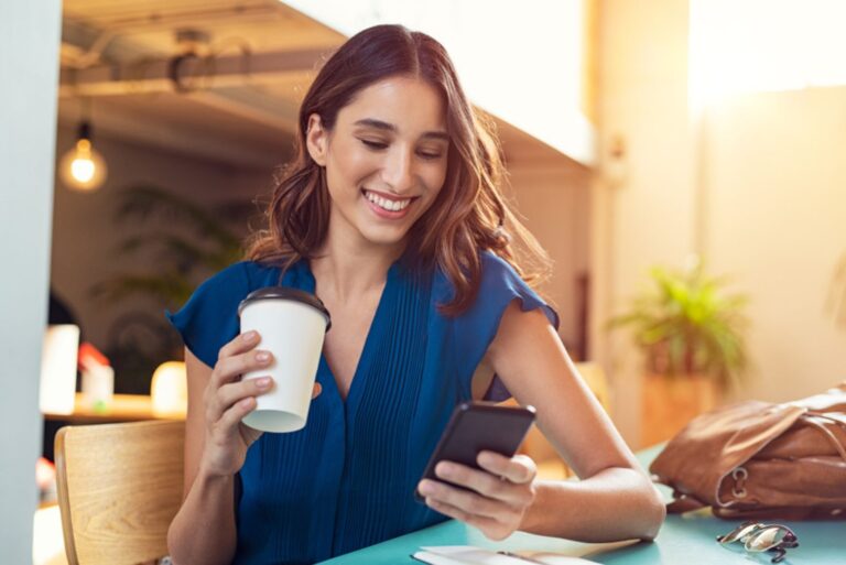 smiling woman texting and holding a cup of coffee