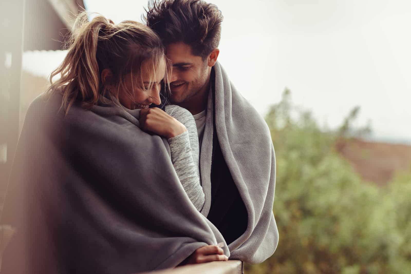 Hombre y mujer juntos en el balcón de una habitación de hotel envueltos en una manta