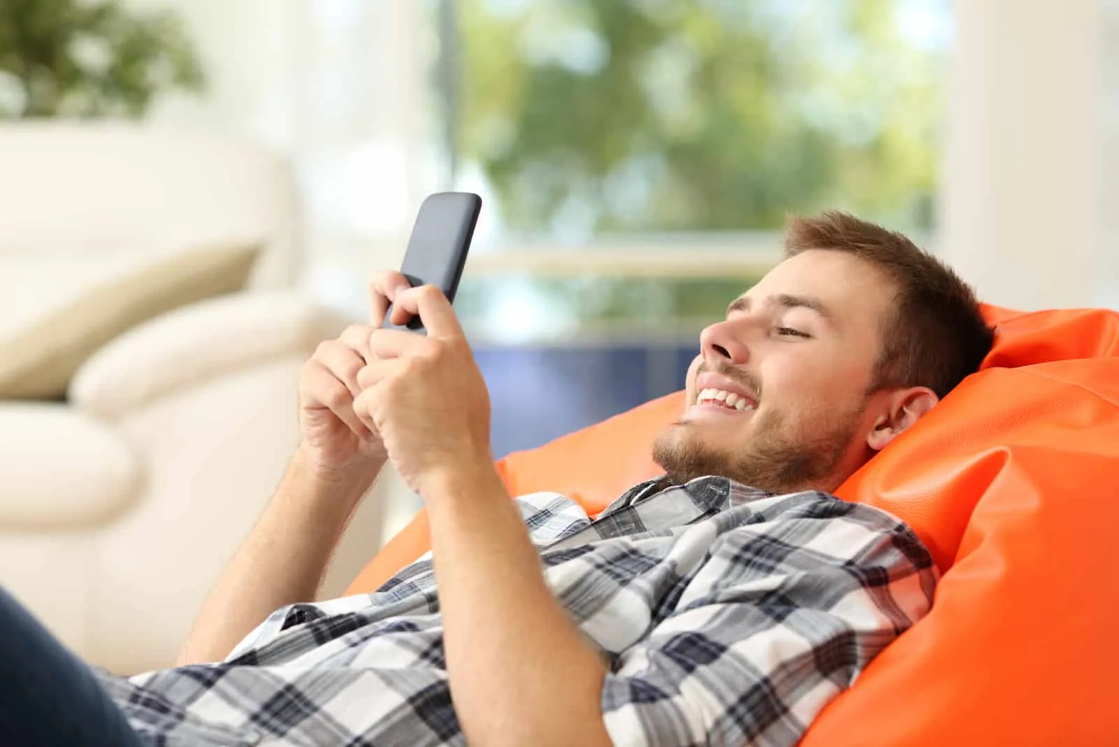 relaxed man using a smartphone lying on an orange pouf